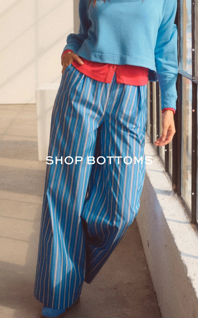 Woman wearing loose white wide-leg linen pants and slide sandals, cropped to show from waist to feet against a neutral background.