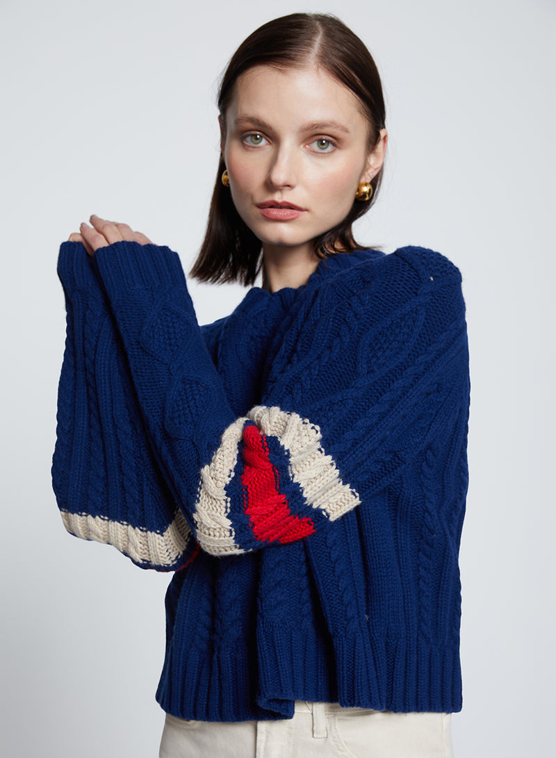 The Felix Cable Knit Sweater in New Navy-model has both of her hands on one side