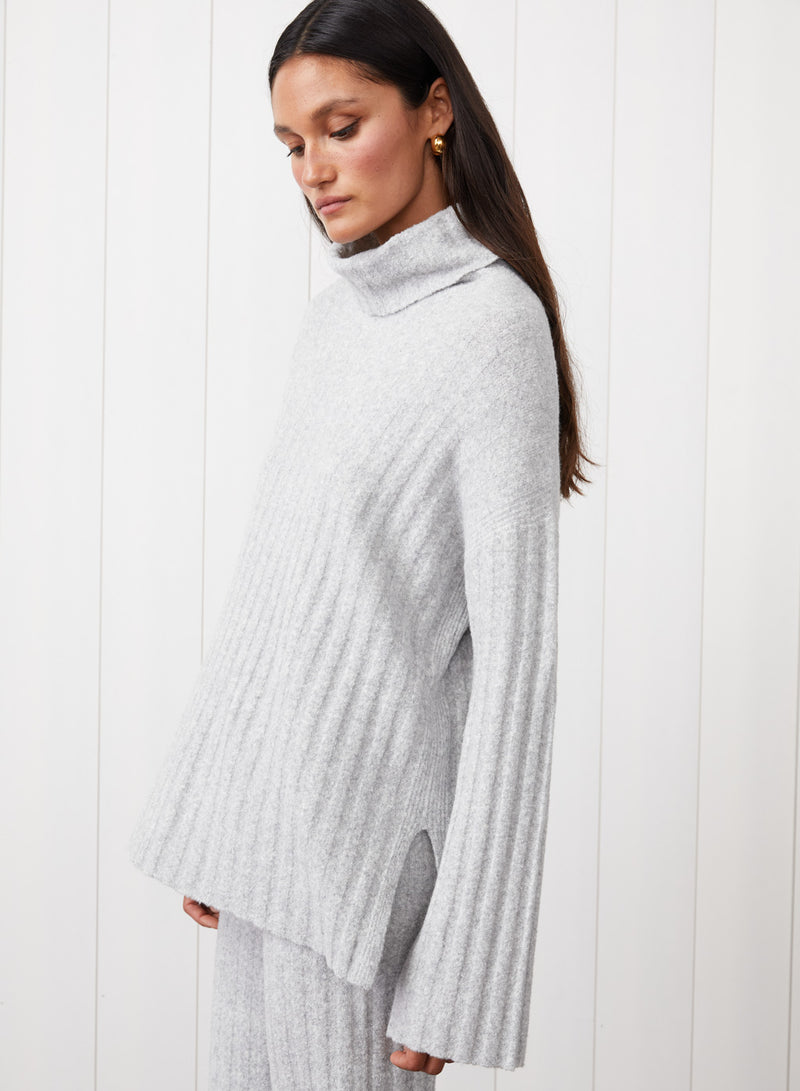 6x6 Rib Turtleneck in Heather Grey - with the model looking down on this side image. Showing the slit on the side as well. 
